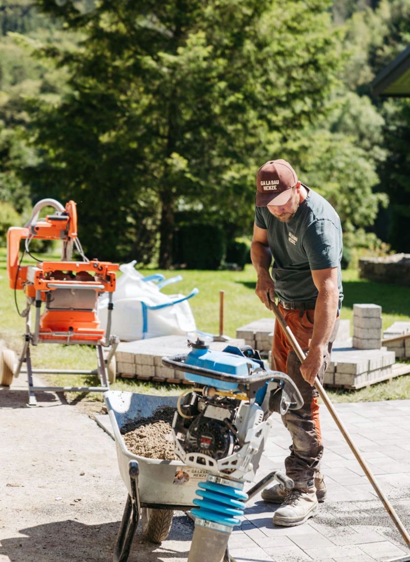 ein-galabau-mitarbeiter-mit-einer-schubkarre-und-einer-ruettelplatte